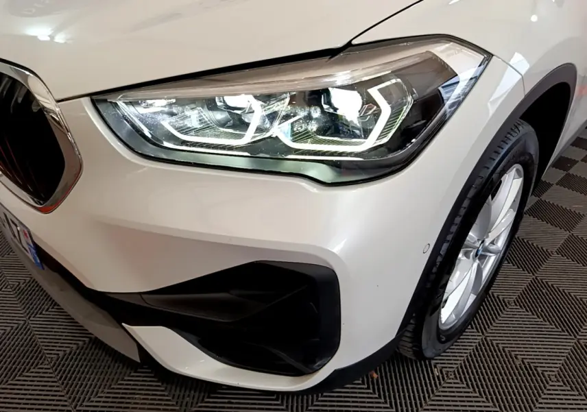 Gros plan sur l'avant droit blanc d'une BMW X1 sDrive18i Lounge 2019, mettant en valeur le phare LED et la jante.