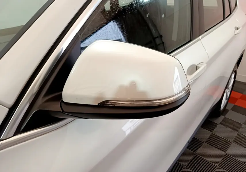 Gros plan sur le rétroviseur droit blanc du BMW X1 sDrive18i Lounge 2019, avec carrosserie blanche visible en arrière-plan.