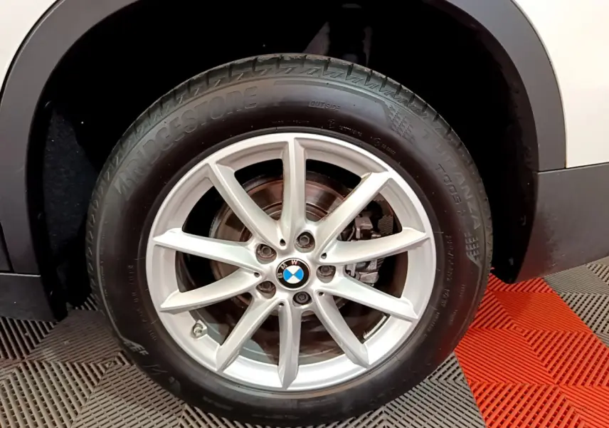 Gros plan sur la roue avant droite d’un BMW X1 blanc, jante alliage argentée et pneu Bridgestone.