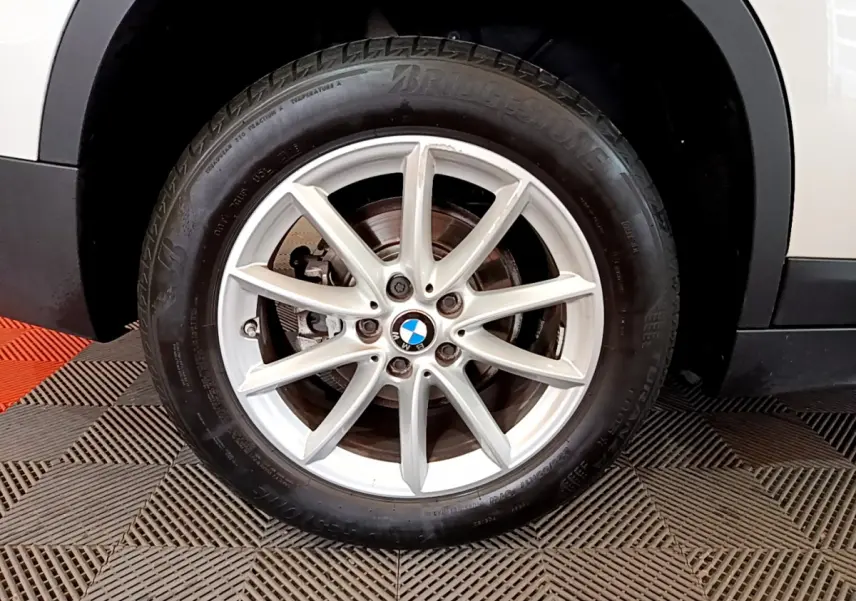 Gros plan sur la roue avant droite blanche d'un BMW X1 sDrive18i Lounge avec jante alliage à 10 branches.