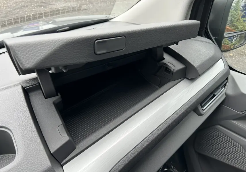 Vue intérieure du Volkswagen Transporter T7 ProCab 2026 montrant la boîte à gants ouverte côté passager avec finition gris clair.