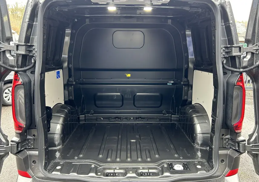 Vue arrière ouverte du Volkswagen Transporter T7 ProCab L1H1 Business en Graphite Dust, montrant l’espace de chargement vide et éclairé.