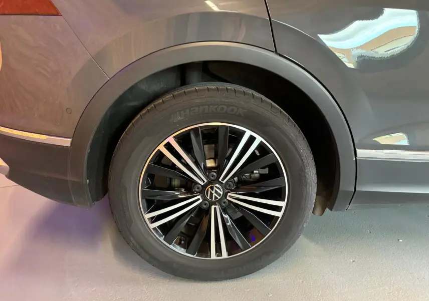 Gros plan sur la roue arrière droite du Volkswagen Tiguan gris 2023 avec jante alliage noire et argent.