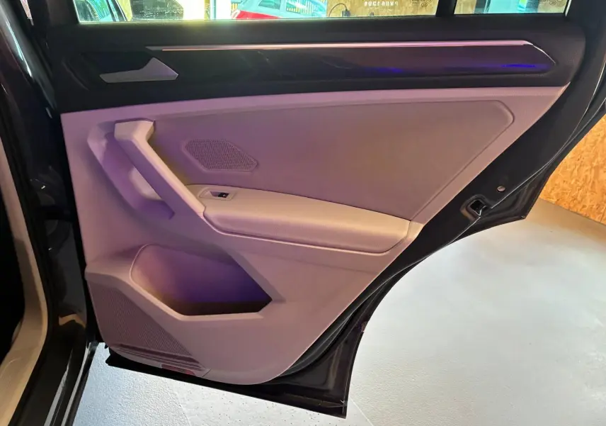 Vue intérieure du panneau de porte arrière gauche gris clair du Volkswagen Tiguan 2023 avec éclairage d'ambiance violet.