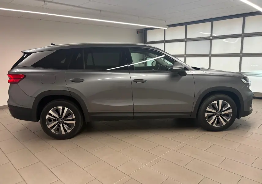 Vue de profil côté gauche d'un Skoda Kodiaq 2025 gris graphite avec jantes alliage et toit noir en intérieur.