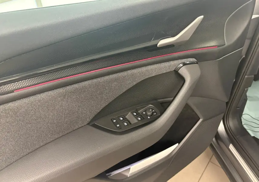 Détail de la porte côté conducteur du Skoda Kodiaq 2025 gris graphite, avec commandes électriques et bande décorative rouge.
