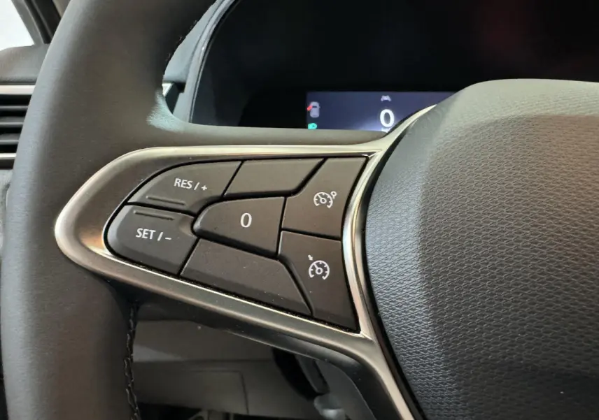 Gros plan sur les commandes du régulateur de vitesse au volant cuir noir de la Renault Clio gris clair 2025 Evolution Blue dCi 100