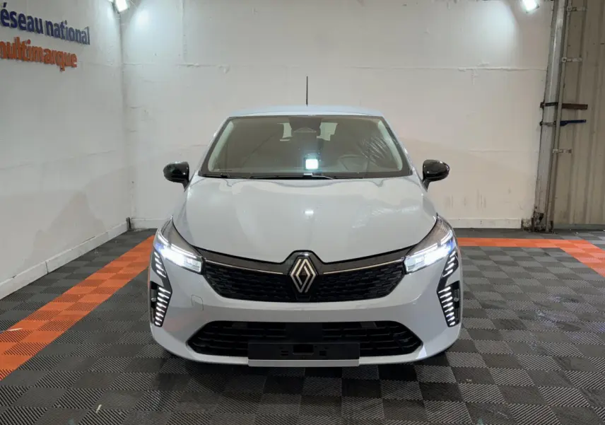 Vue frontale d'une Renault Clio gris clair 2025 avec feux LED allumés dans un garage éclairé.