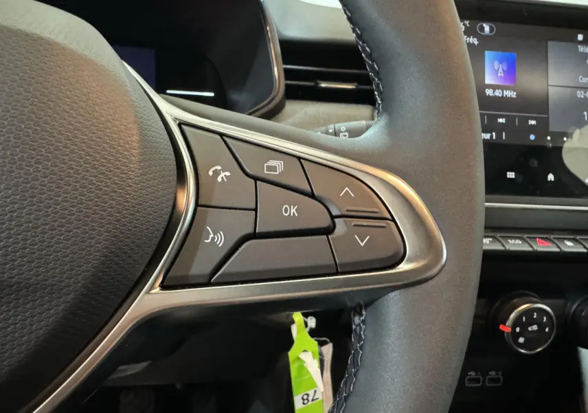 Gros plan sur les commandes au volant cuir noir de la Renault Clio gris clair, avec écran tactile en arrière-plan.