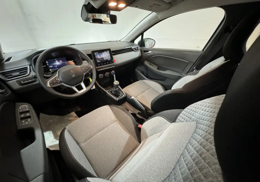 Intérieur de Renault Clio 2025 vu côté conducteur, sièges gris clair et tableau de bord avec écran tactile central.