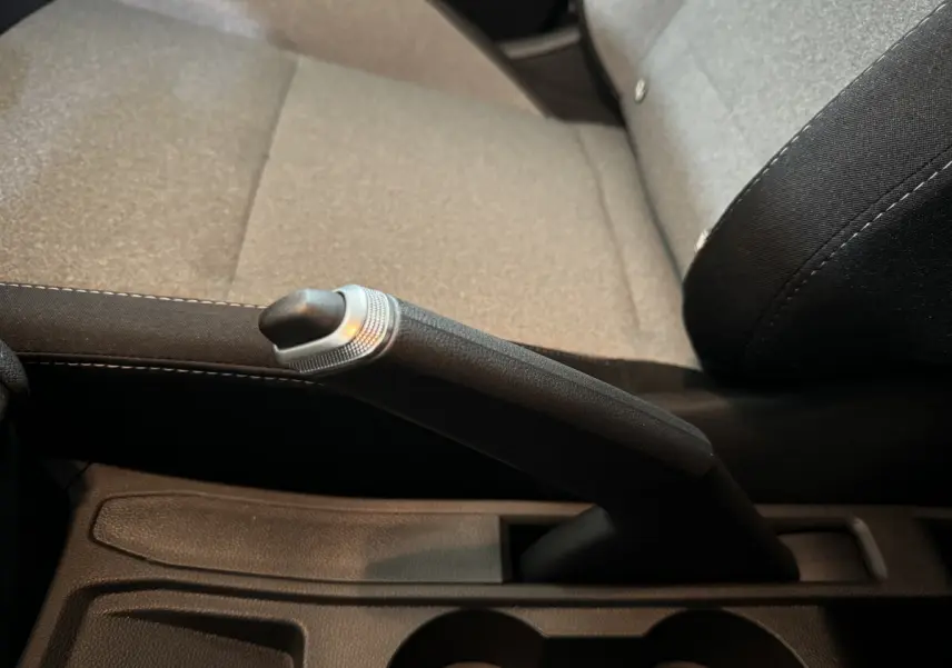 Le levier de frein à main noir en gros plan, avec la sellerie grise et noire de la Renault Clio Evolution 2025 visible en arrière-plan.