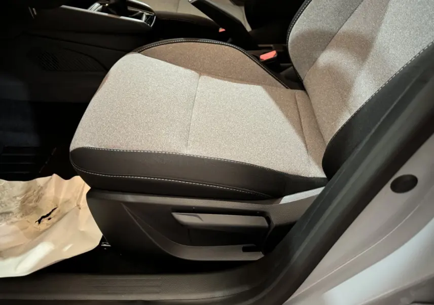 Gros plan sur le siège avant droit gris clair de la Renault Clio Evolution Blue dCi 100 2025 avec volant et console partiellement visibles.