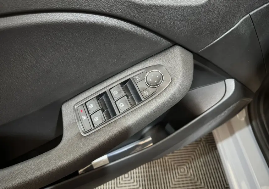Gros plan sur la commande des vitres électriques côté conducteur d'une Renault Clio gris clair, porte ouverte.