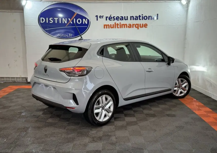 Renault Clio gris clair vue 3/4 arrière droit en intérieur avec feux arrière allumés et jantes alliage.