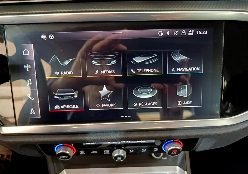 Écran tactile central de l'Audi Q3 noir, vue rapprochée du tableau de bord avec commandes climatisation visibles.