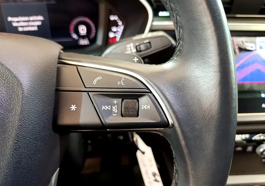 Gros plan sur les commandes gauche du volant cuir noir de l'Audi Q3 35 TDI 2021 avec écran de caméra de recul visible.