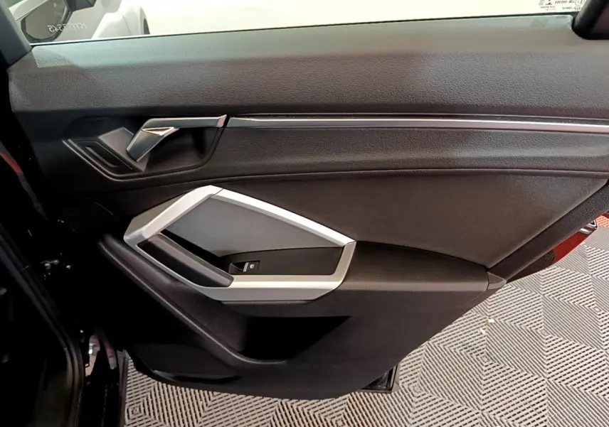 Vue intérieure du panneau de porte côté gauche de l'Audi Q3 noir, avec poignée argentée et commande de vitre.