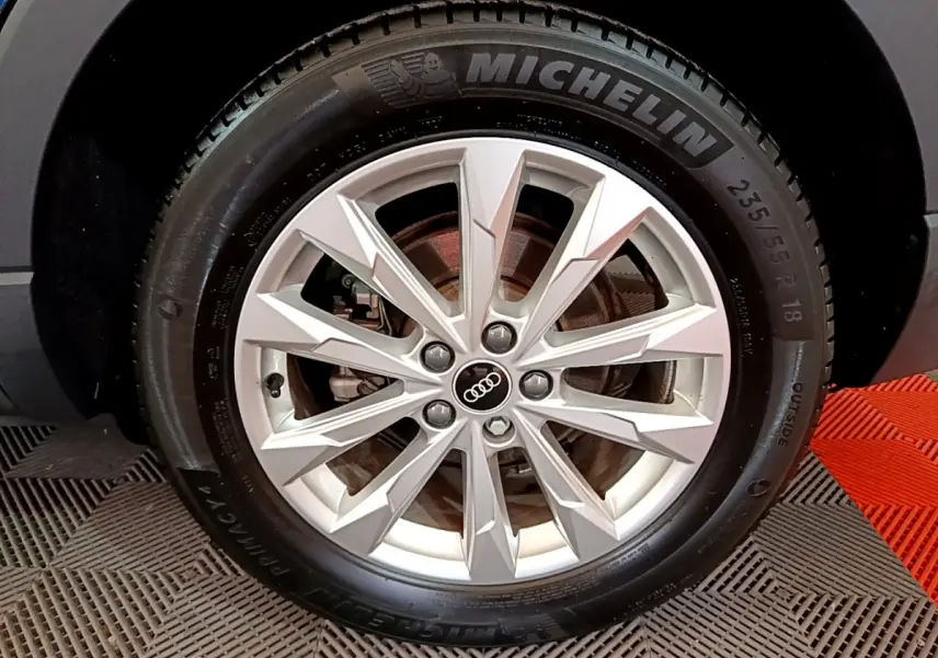 Gros plan sur la jante alliage argentée avec logo Audi au centre, pneu Michelin monté sur Audi Q3 noir.