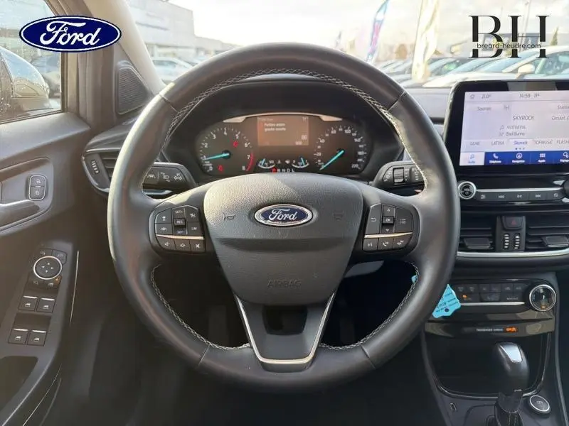 Vue intérieure centrée sur le volant cuir multifonction du Ford Puma gris avec tableau de bord et écran tactile visible.
