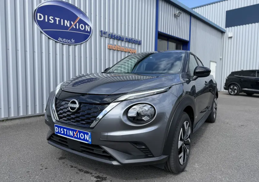 Nissan Juke Hybrid gris squale métal en 3/4 avant droit, avec calandre noire et phares ronds distinctifs.