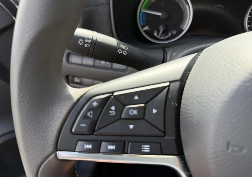 Gros plan sur les commandes multifonctions noires à gauche du volant gris du Nissan Juke Hybrid 2025, tableau de bord en arrière-plan.