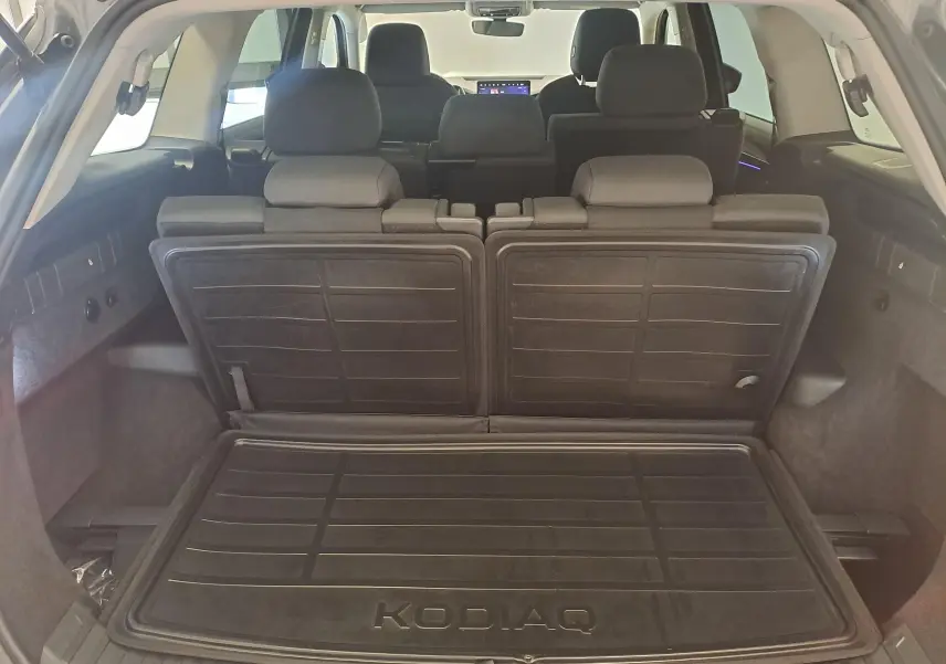 Vue intérieure du coffre du Skoda Kodiaq gris graphite 2025, avec sièges arrière relevés et tapis de coffre marqué KODIAQ.