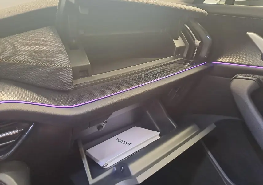 Intérieur du Skoda Kodiaq 2025 en gris graphite, vue sur la boîte à gants ouverte et l’éclairage d’ambiance violet.