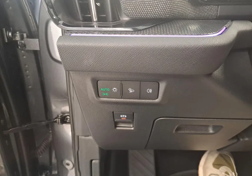 Détail intérieur côté gauche du tableau de bord gris graphite du Skoda Kodiaq 2025 avec commandes d’éclairage et frein à main électrique.