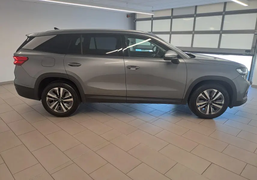 Vue de profil côté gauche d'un Skoda Kodiaq gris graphite 2025 en intérieur, avec jantes alliage et vitres teintées.