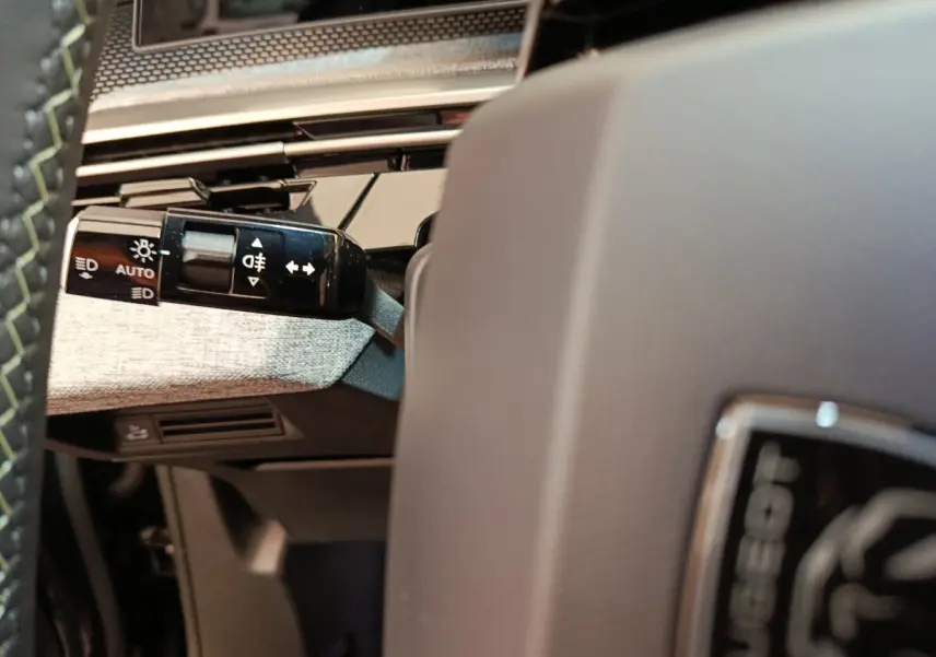 Détail du commodo d'éclairage à gauche du volant gris clair dans l'habitacle du Peugeot 3008 gris foncé 2025.