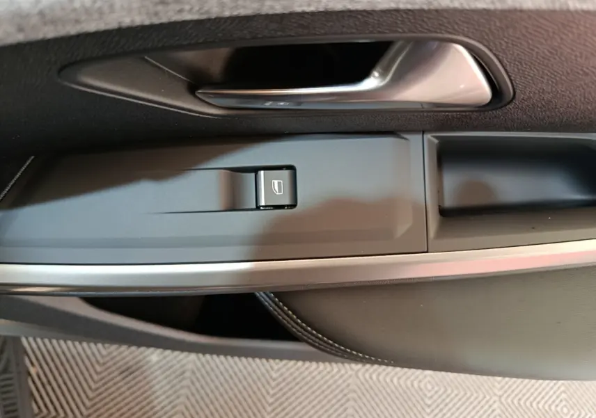 Poignée de porte intérieure côté conducteur du Peugeot 3008 gris foncé, avec bouton de commande de vitre électrique.
