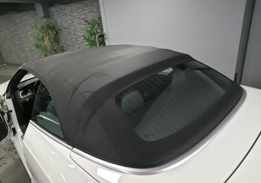 Vue arrière côté gauche d'un Audi A5 Cabriolet blanc avec capote noire fermée dans un garage.