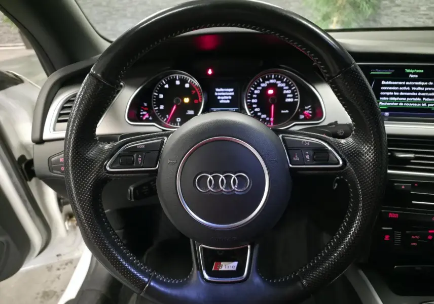 Vue rapprochée du volant sport en cuir perforé S line d'une Audi A5 Cabriolet blanc, avec tableau de bord et écran MMI visibles.