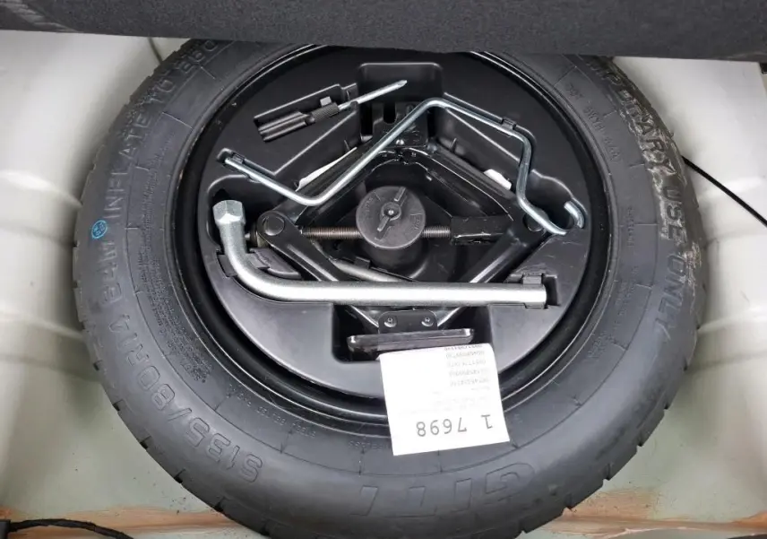 Roue de secours avec outils de changement visibles dans le coffre d'une FIAT 500 blanche Bossa Nova.