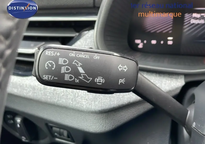 Gros plan sur la commande de régulateur de vitesse au volant d’une Skoda Scala blanc glacier, tableau de bord en arrière-plan flou.