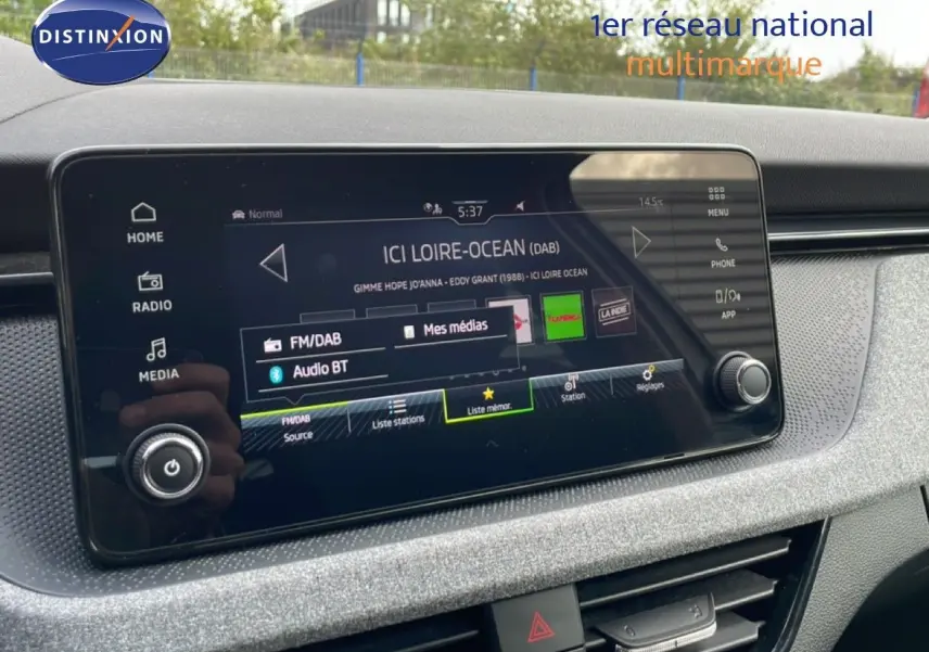 Écran tactile central de la Skoda Scala blanc glacier, affichant la radio FM/DAB avec interface moderne et commandes tactiles.
