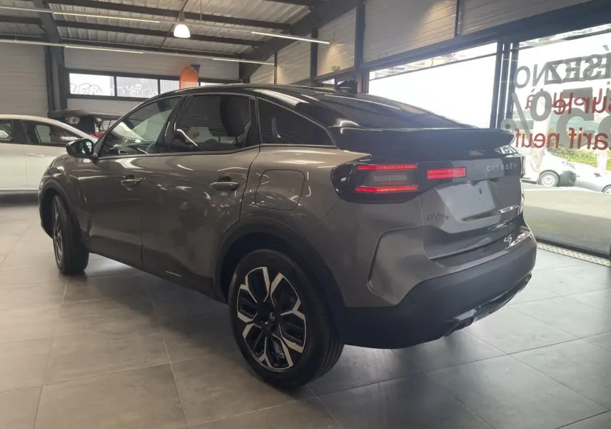 Vue 3/4 arrière droite d'une Citroën C4 grise avec toit noir et feux arrière LED allumés en showroom.