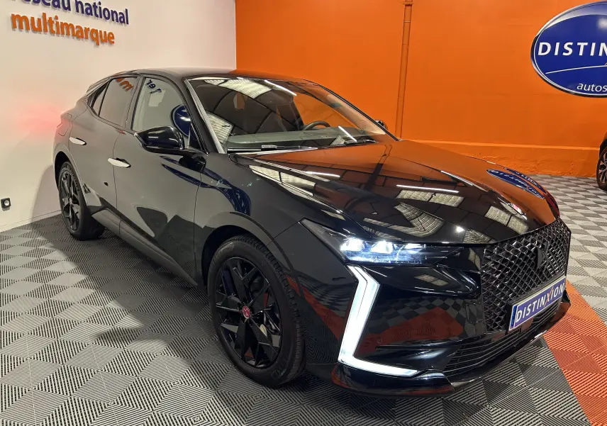 Vue 3/4 avant d'une DS4 noire Perla Nera avec phares LED et calandre distinctive dans un showroom orange.