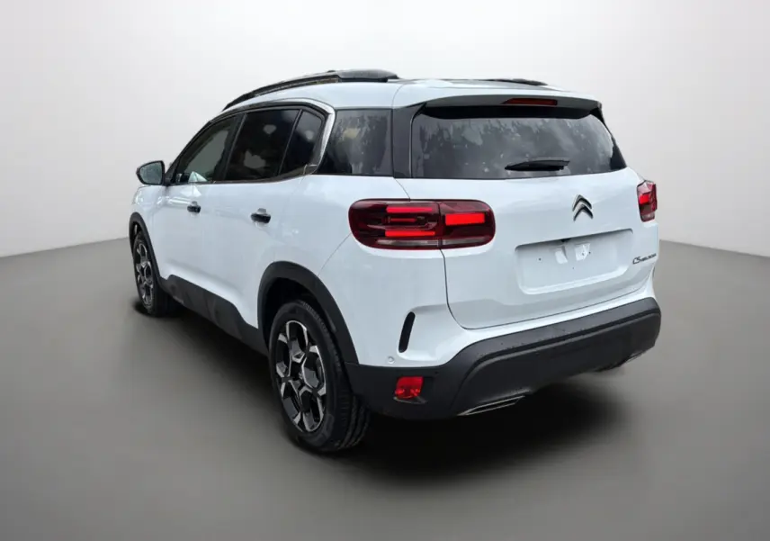 Vue 3/4 arrière droite d’un Citroën C5 Aircross Hybrid blanc okénite avec barres de toit et vitres surteintées.