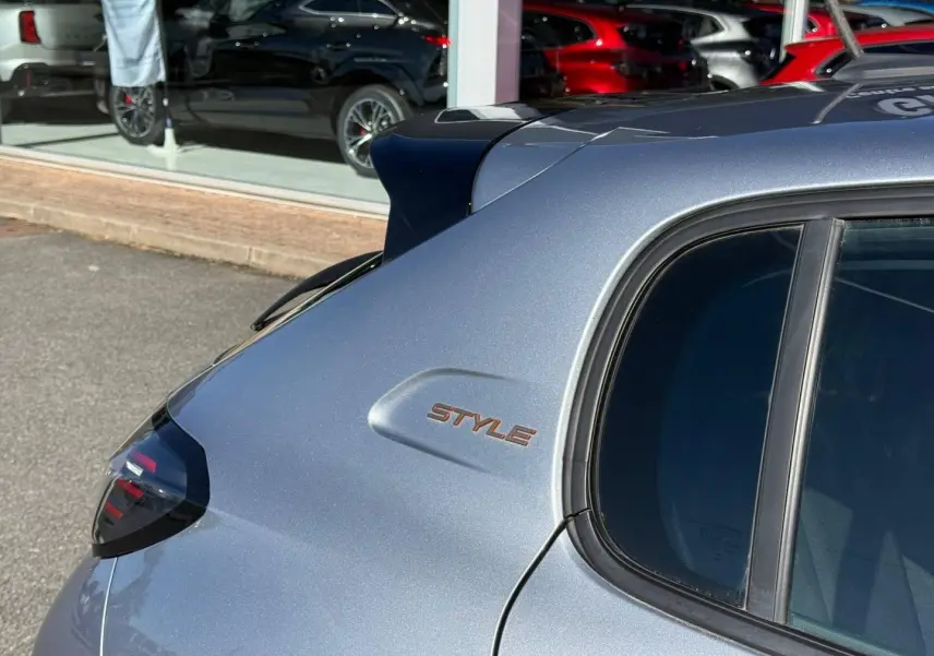 Vue arrière côté gauche d'une Peugeot 208 gris Artense avec logo Style sur la custode et vitres teintées.