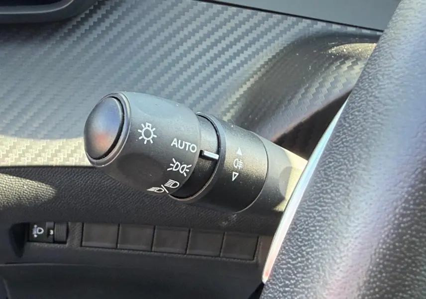 Gros plan sur la commande des phares avec finition effet carbone et volant partiel gris dans une Peugeot 208 gris Artense.