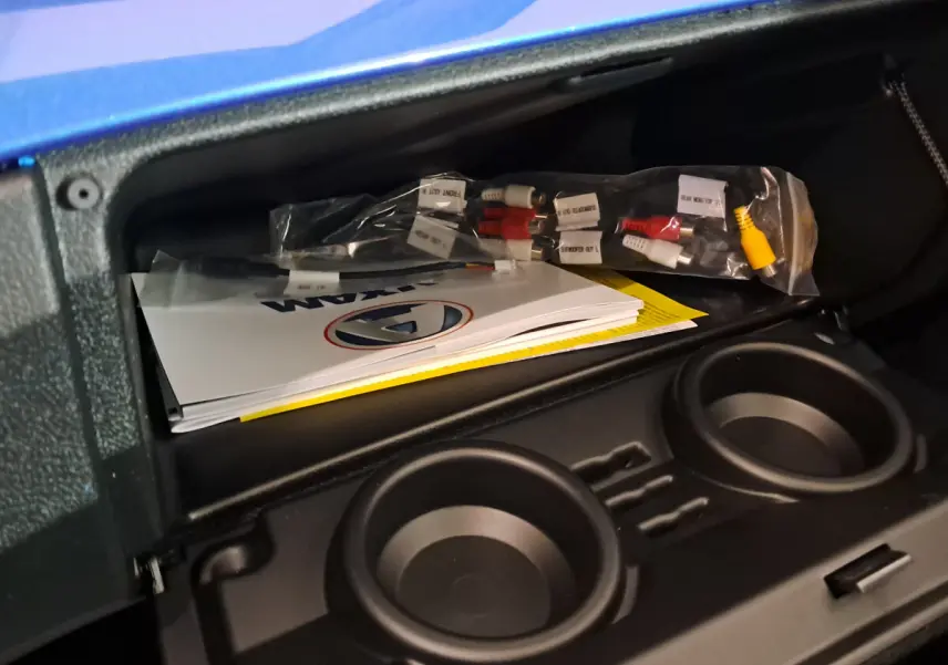 Coffre ouvert de l'AIXAM AMBITION bleu 2025 montrant des manuels et câbles, avec porte-gobelets intégrés.