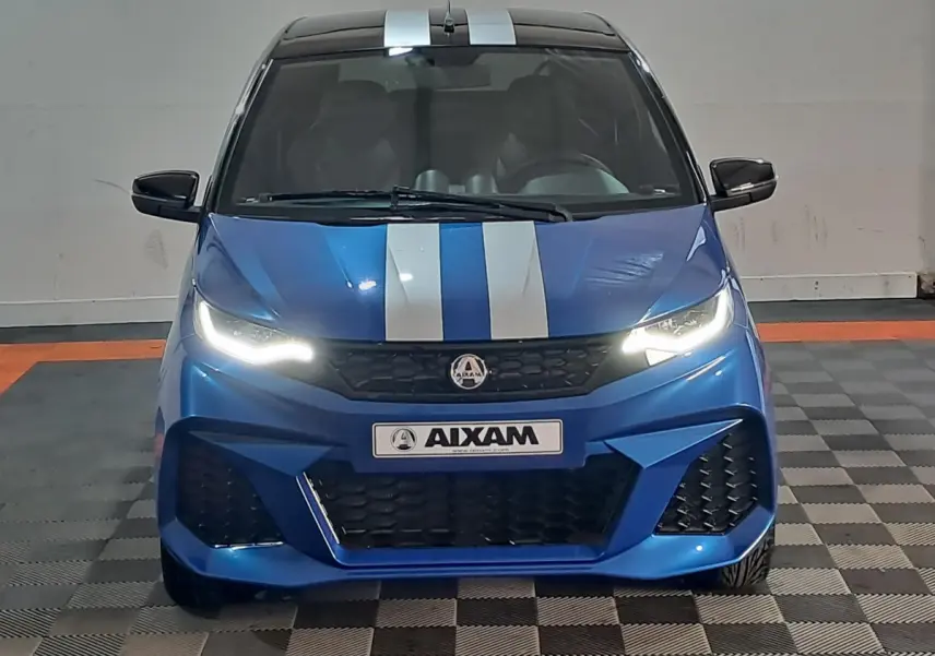 Vue frontale d'une Aixam Ambition 0.5 City GTO bleue avec bandes blanches et phares allumés dans un garage.
