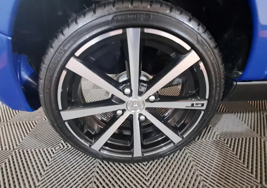 Gros plan sur la jante noire et argentée avec logo Aixam et inscription GT, sur roue avant droite d'une Aixam Ambition bleue.