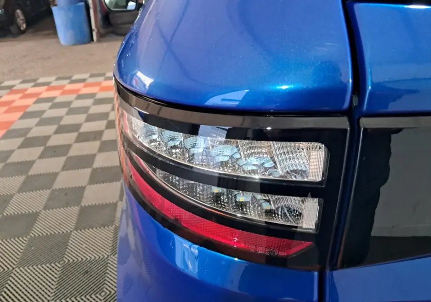 Gros plan sur le feu arrière gauche bleu d'une Aixam Ambition 2025 avec détails lumineux et carrosserie brillante.