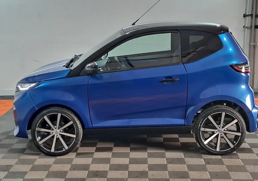 Vue de profil côté gauche d'une Aixam Ambition 0.5 City GTO bleu avec toit noir et jantes noires à rayons.