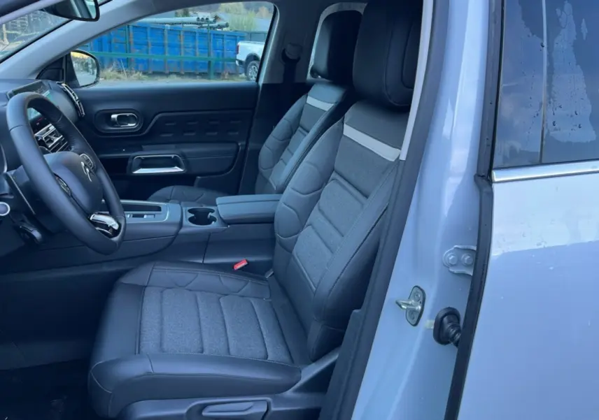 Vue intérieure côté conducteur du Citroën C5 Aircross blanc okénite, montrant les sièges avant en cuir et tissu gris.