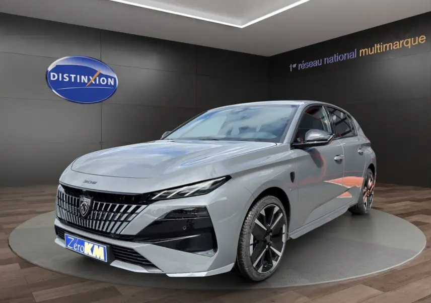 Peugeot 308 gris clair vue 3/4 avant avec calandre distinctive et jantes noires en showroom.