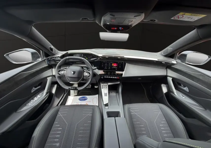 Vue intérieure avant de la Peugeot 308 2026, sièges noirs, tableau de bord moderne avec écran tactile central.
