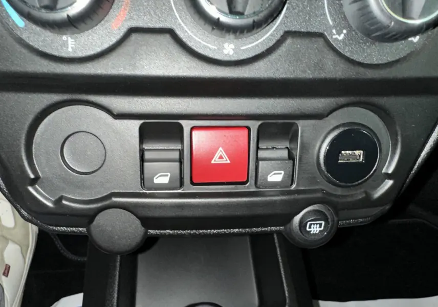 Gros plan sur la console centrale noire de l'AIXAM AMBITION rouge 2025, avec boutons de vitres et alerte au centre.